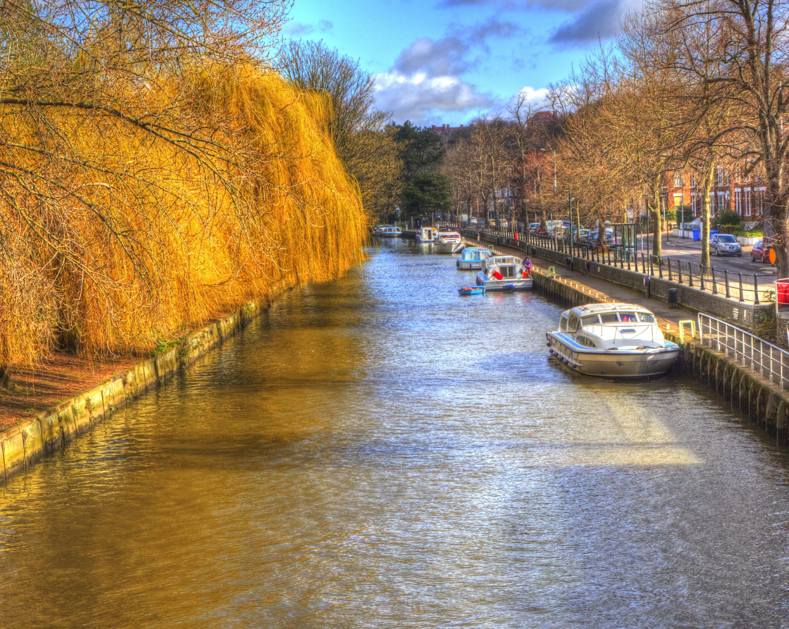 Boats moored along a tree-lined river in autumn sunshine